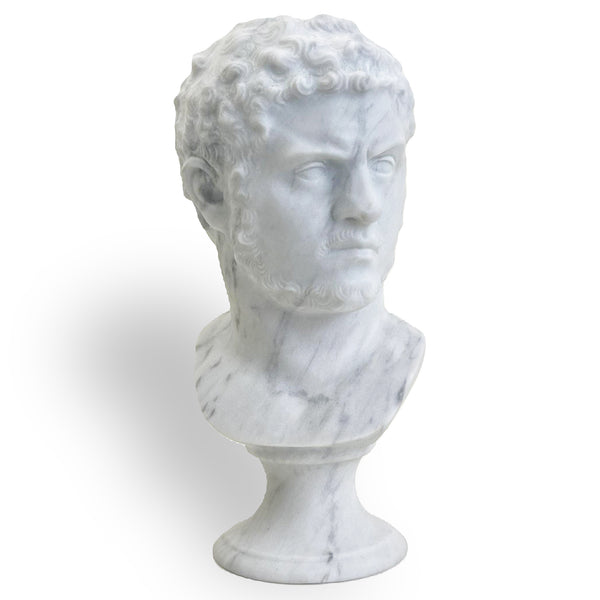 Buste de l’empereur Caracalla en marbre blanc, avec des cheveux bouclés, une barbe courte et un regard sévère tourné de côté, sur un piédestal clair