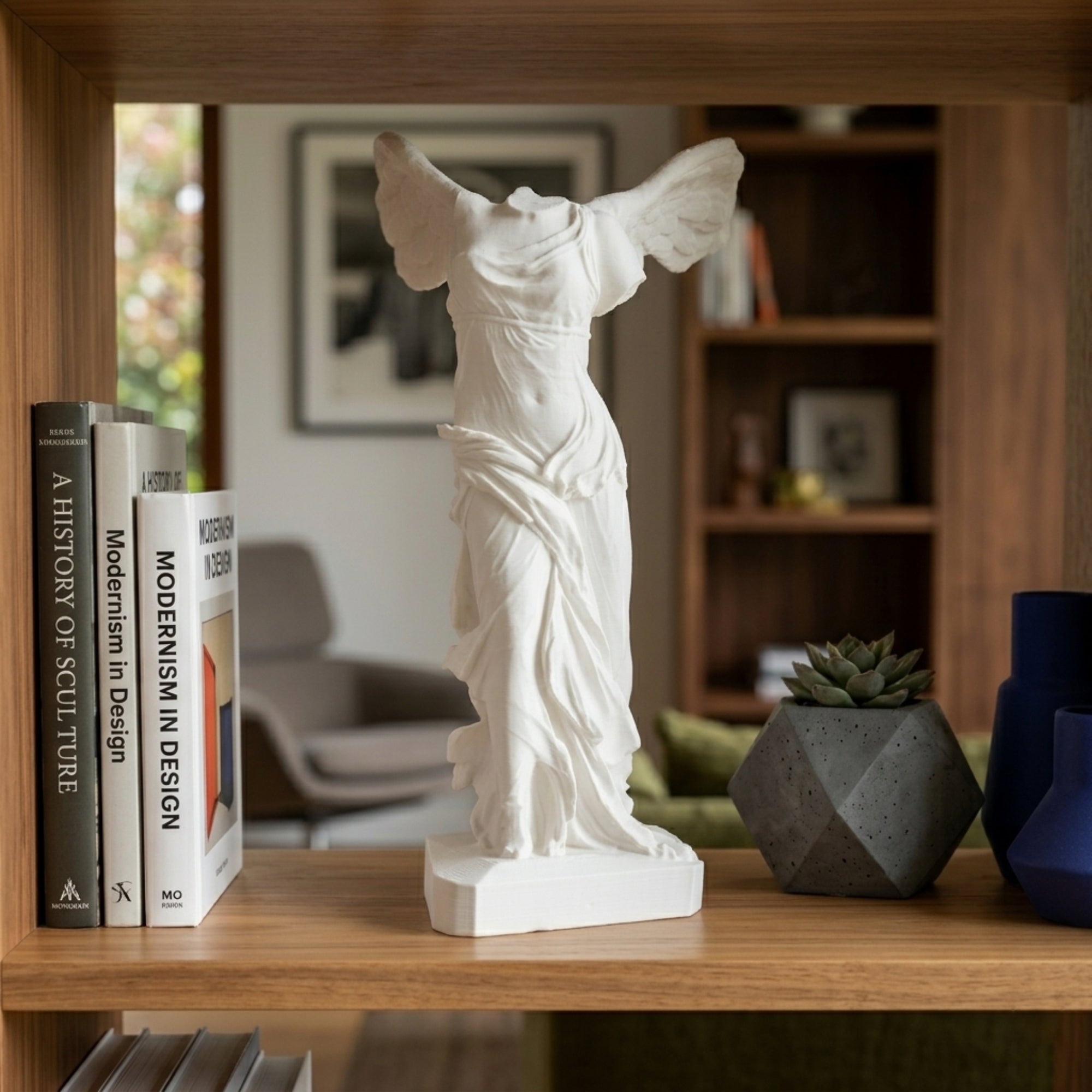 Replica 3D della Vittoria Alata su una scrivania in legno con pianta e libri.