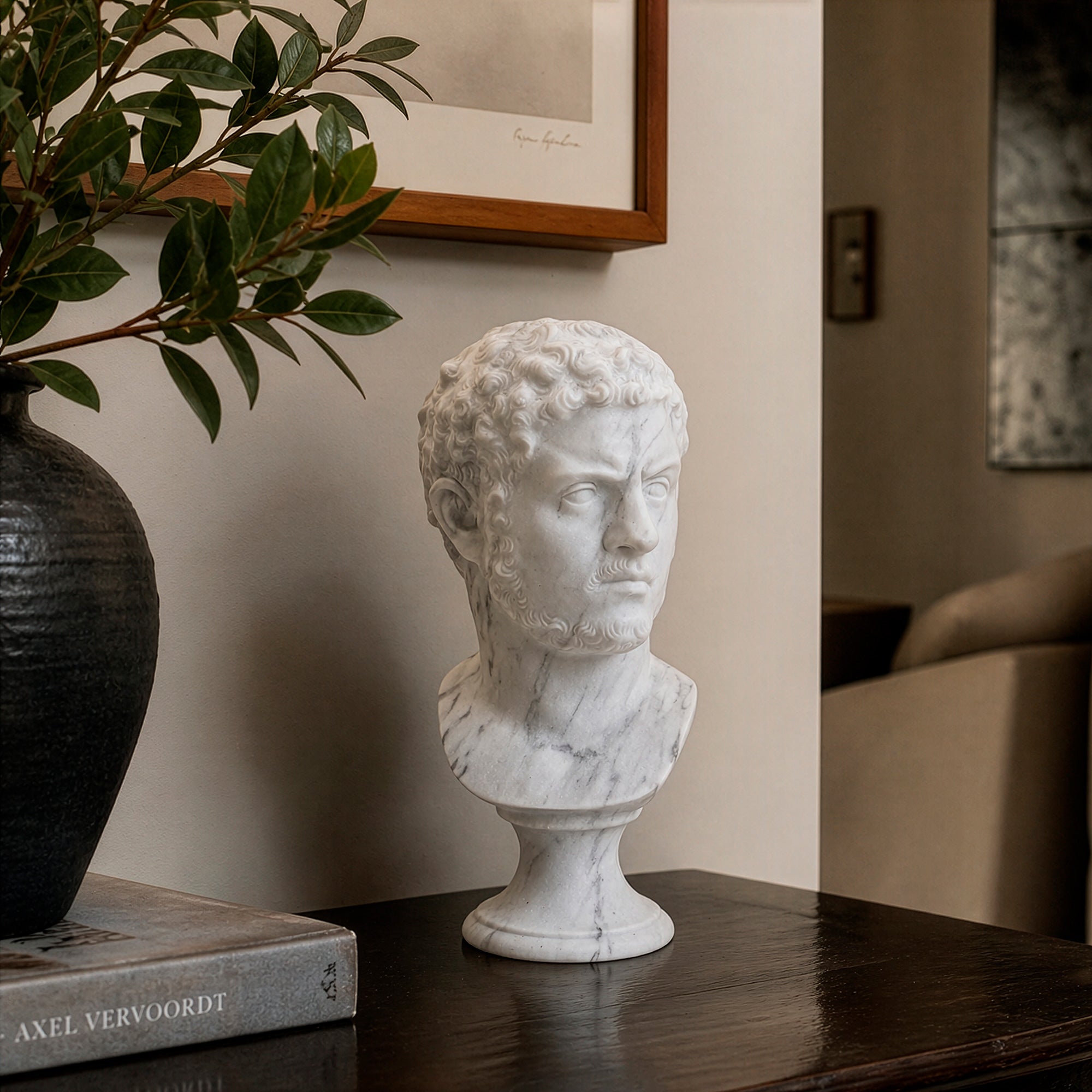 Busto dell’imperatore Caracalla in marmo bianco, con capelli ricci, barba corta e sguardo severo rivolto di lato, su piedistallo chiaro