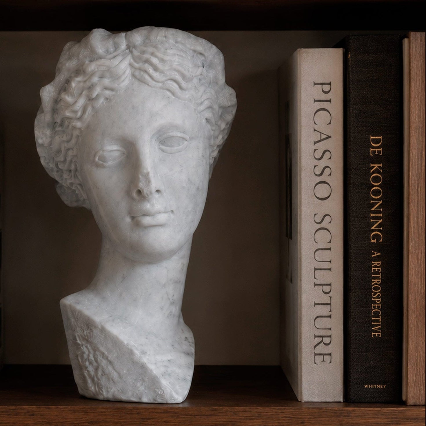 Bust of Thalia, Muse of Comedy, in white Carrara marble, front view in a library.