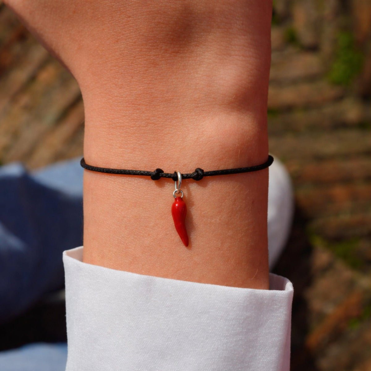 Bracciale con cordoncino nero e piccolo corno rosso, indossato al polso accanto a una camicia bianca