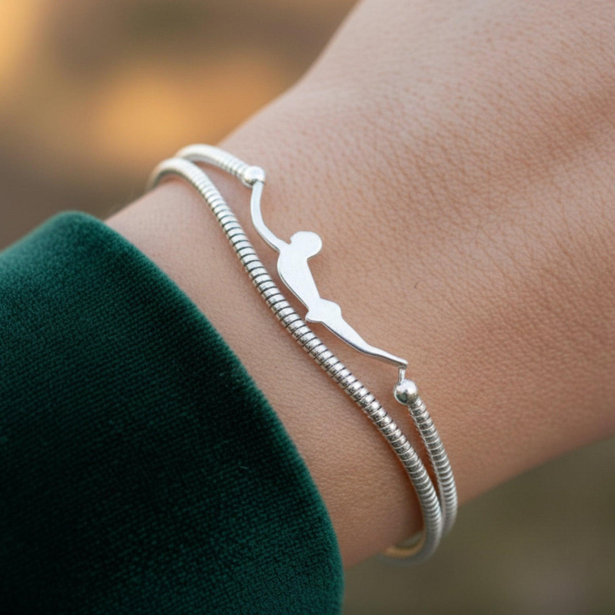 Bracciale in argento con sagoma del Tuffatore di Paestum, indossato al polso accanto a una manica verde