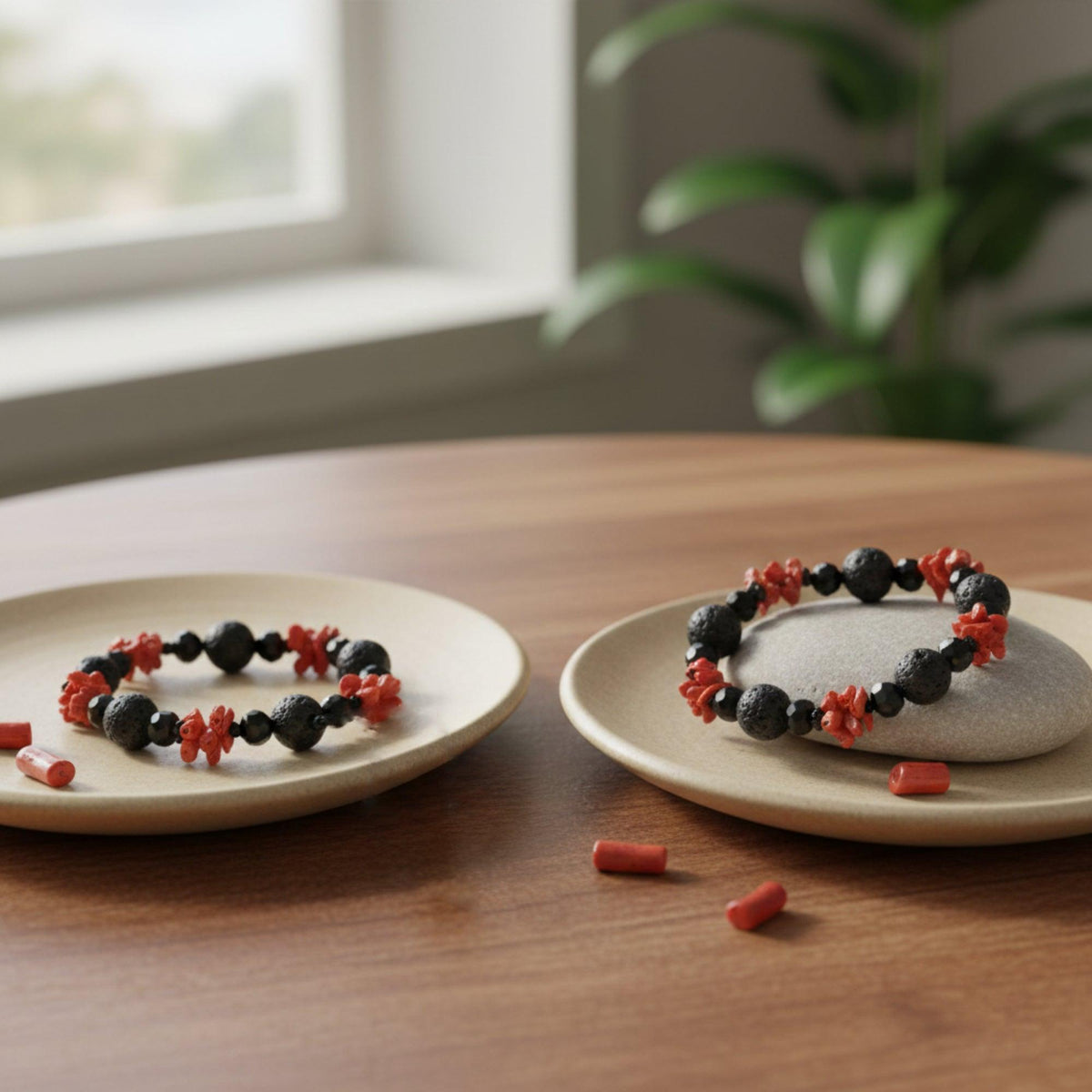 Due bracciali in corallo rosso, pietra lavica e onice su piatti chiari, su un tavolo di legno