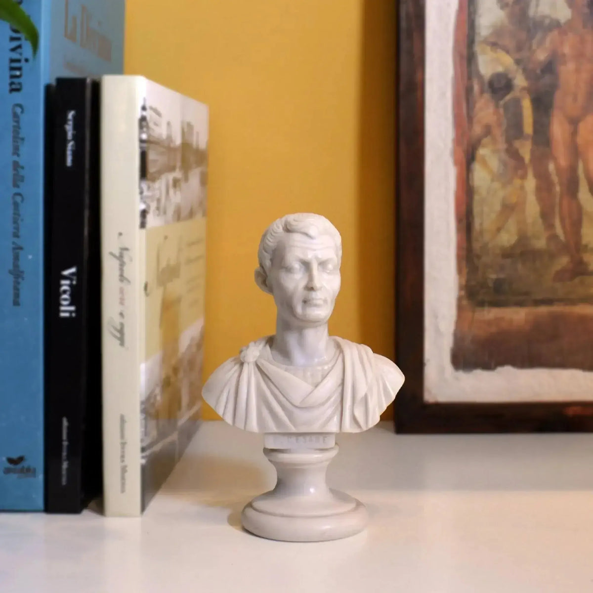 Busto di Giulio Cesare in marmo di Carrara ricomposto, su un ripiano accanto a libri e a un quadro.