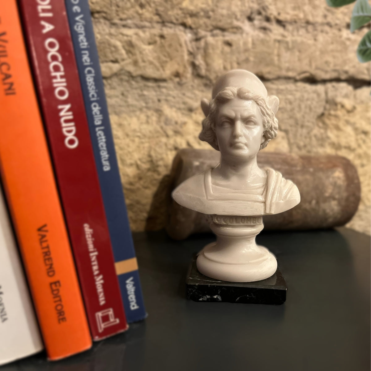 Busto di Cristoforo Colombo in alabastro ricomposto, accanto a libri su un ripiano scuro