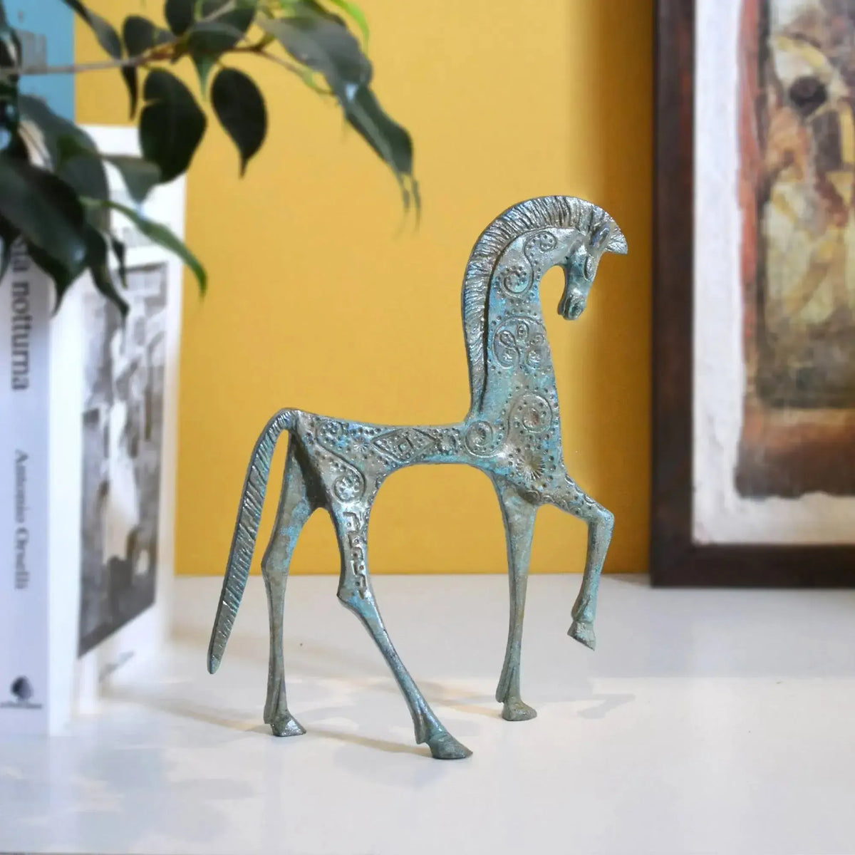 Cavallo greco in bronzo su un piano bianco, accanto a libri e un quadro