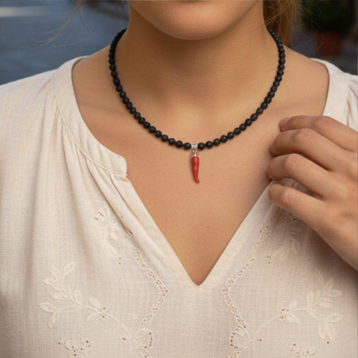 Collana in pietra lavica con corno di corallo rosso, dettaglio indossato su camicia chiara