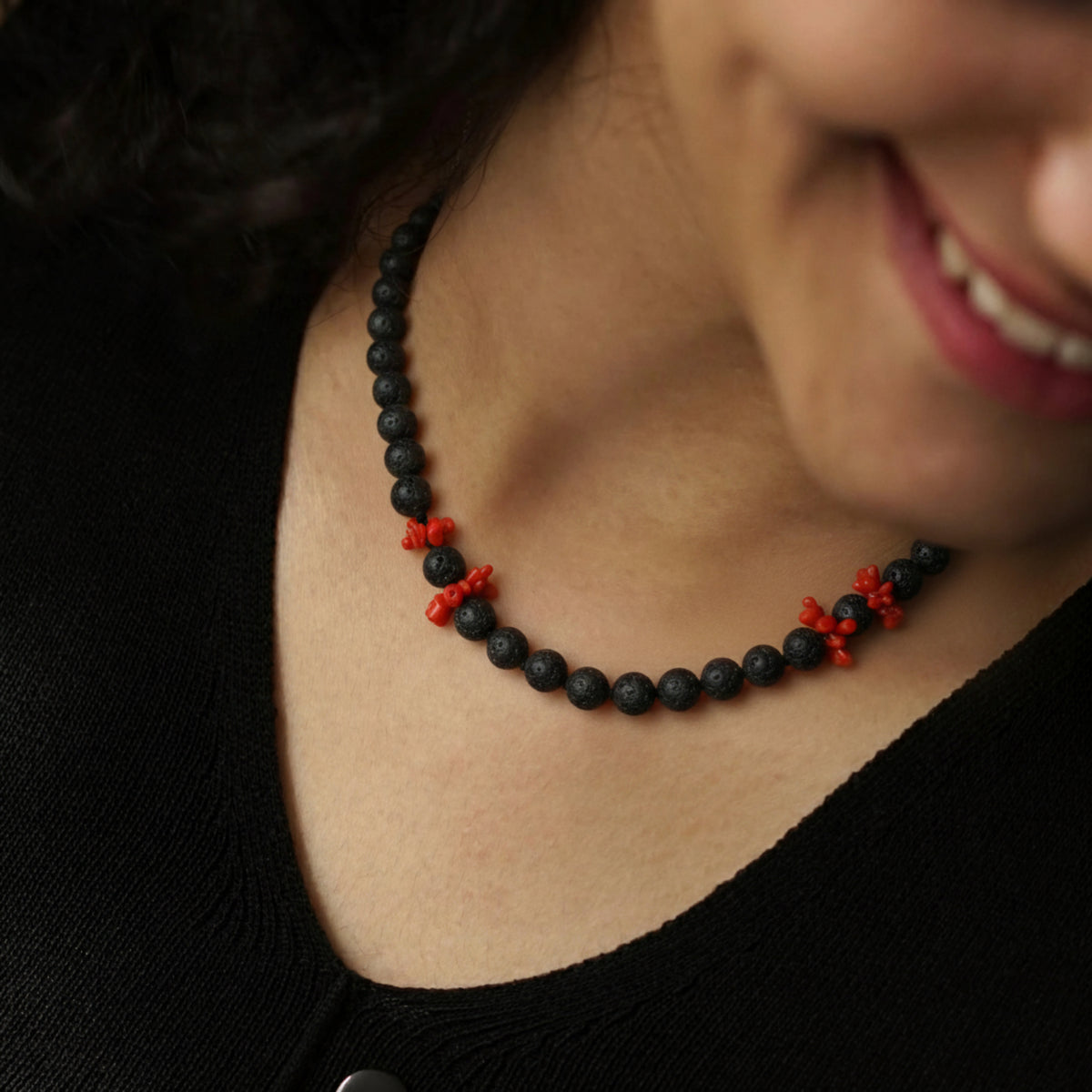 Collana in pietra lavica con gruppi di corallo rosso indossata su una maglia nera