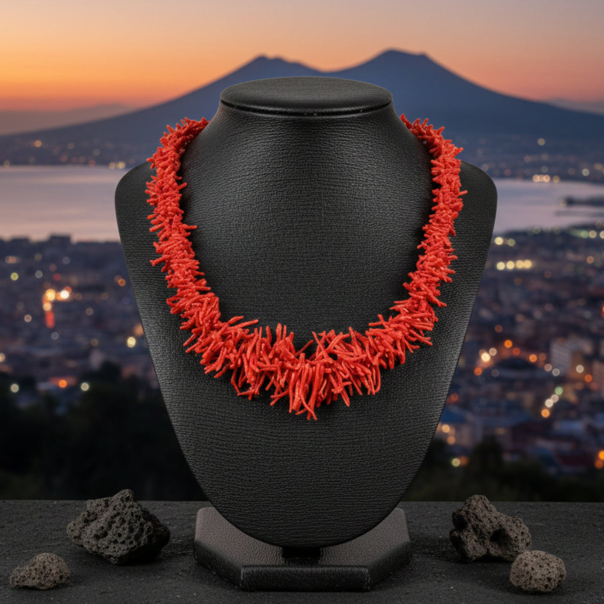 Collana di rami di corallo rosso su espositore nero, con mare e montagna sullo sfondo