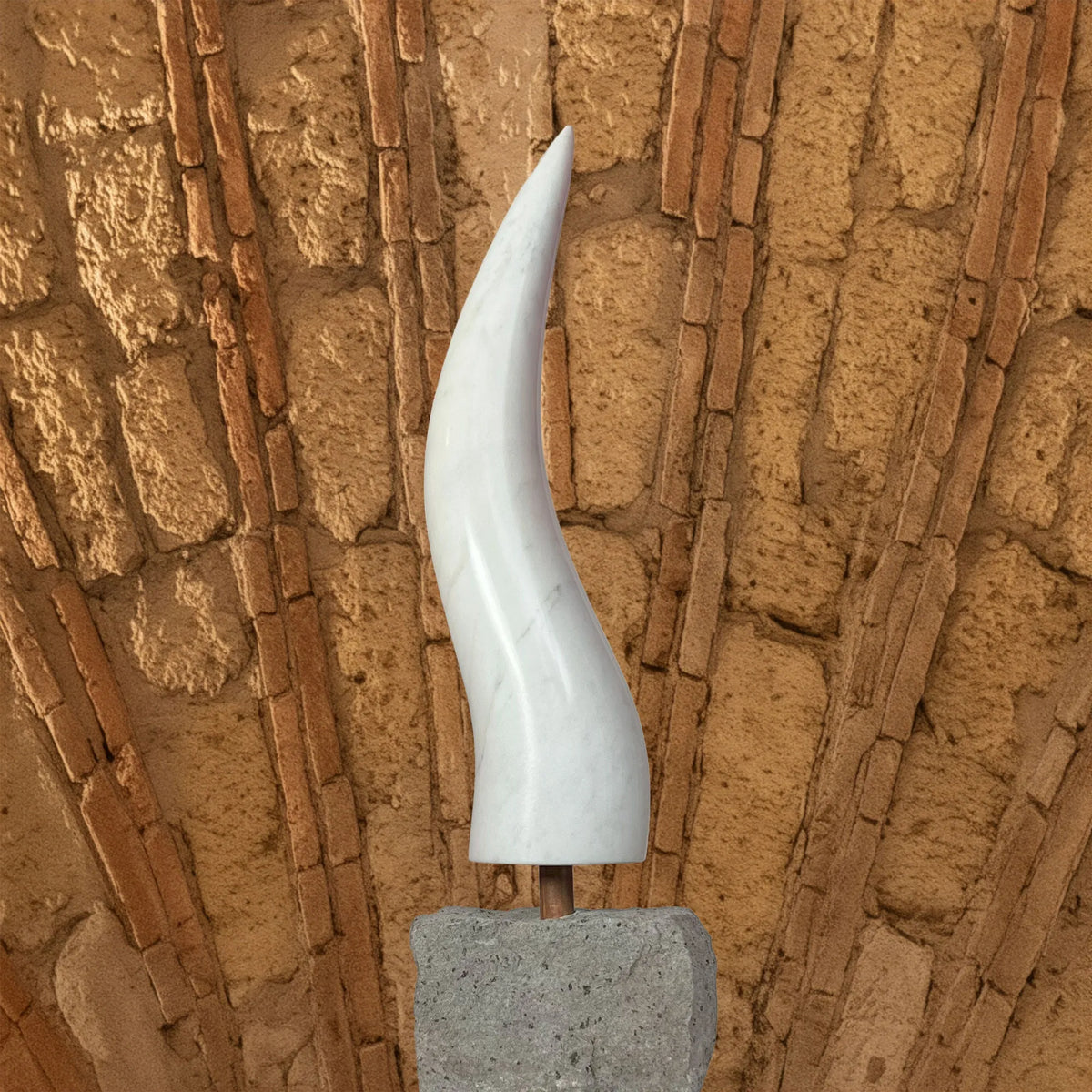 Corno in marmo di Carrara con base in pietra chiara davanti a un muro in mattoni