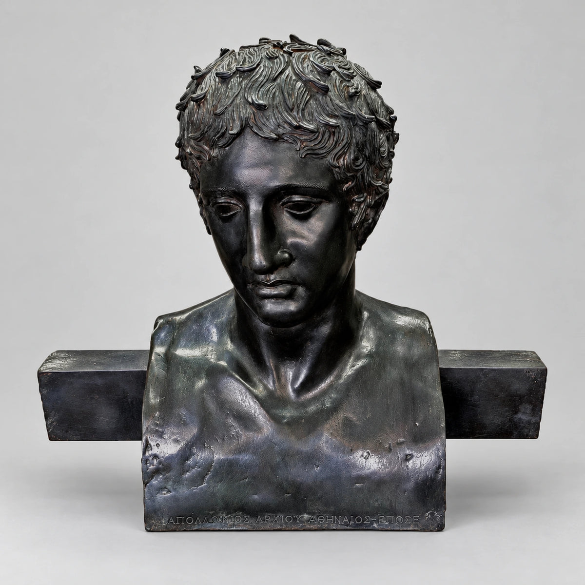 Erma di Doriforo, busto in bronzo con patina scura, vista frontale su sfondo grigio chiaro con luce morbida.