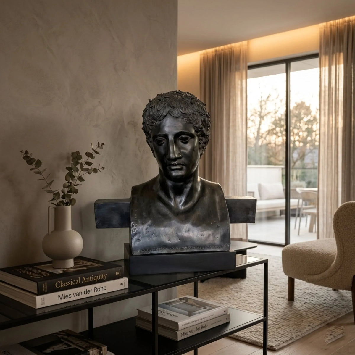 Erma di Doriforo in bronzo scuro su una console con libri e vaso, in un soggiorno con poltrona.