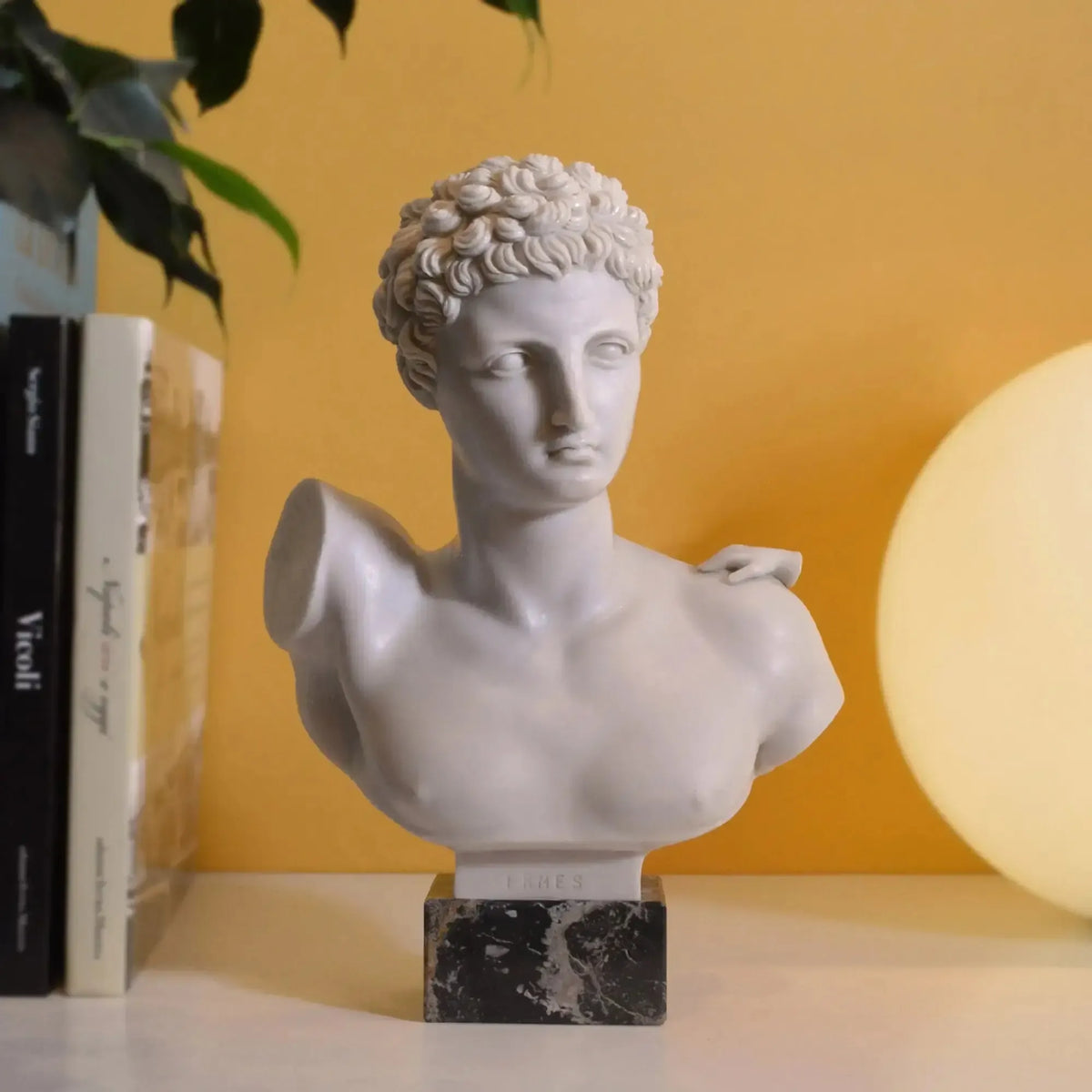 Busto di Hermes in marmo vista frontale vicino i libri