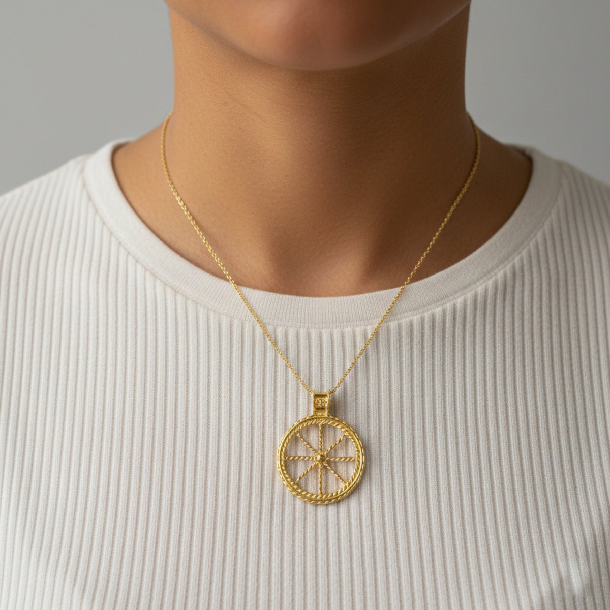 Pendente dorato a forma di ruota con catenella, indossato su una maglia bianca
