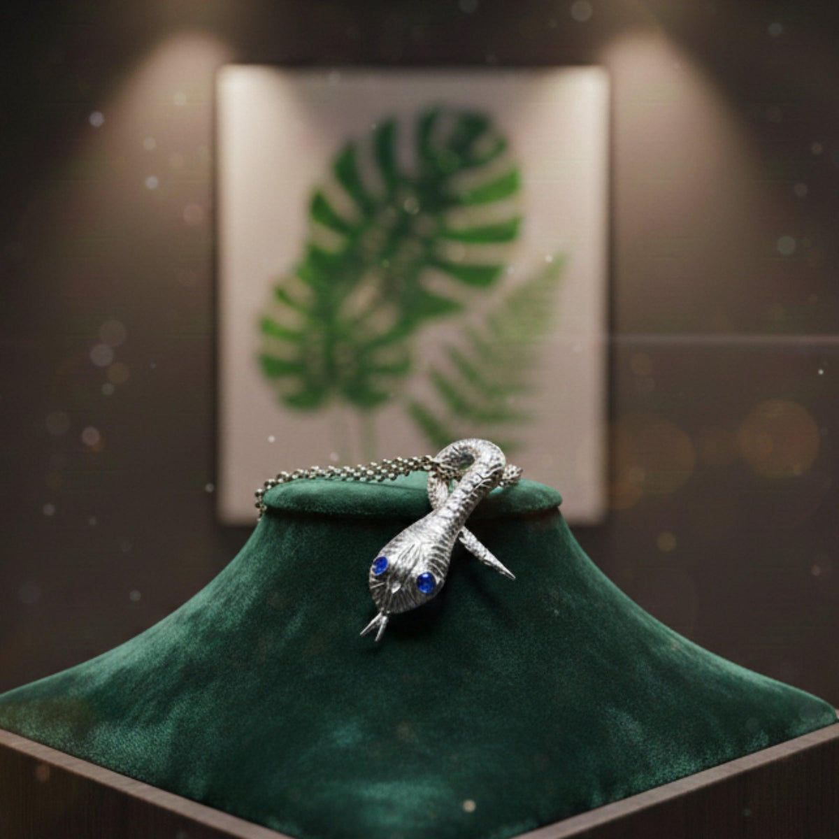 Pendente Serpentello in argento con occhi blu, su un espositore verde