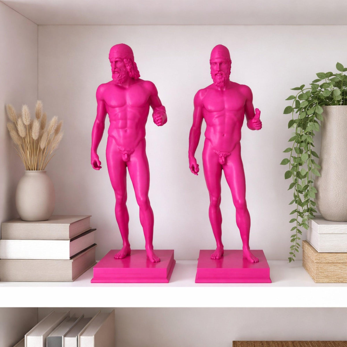 Due riproduzioni dei Bronzi di Riace in PLA magenta su una mensola, tra libri e vasi con piante.