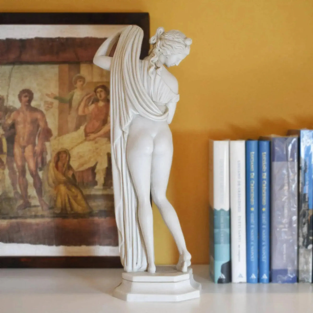 Venere Callipigia in marmo vista da dietro, accanto a libri e un quadro