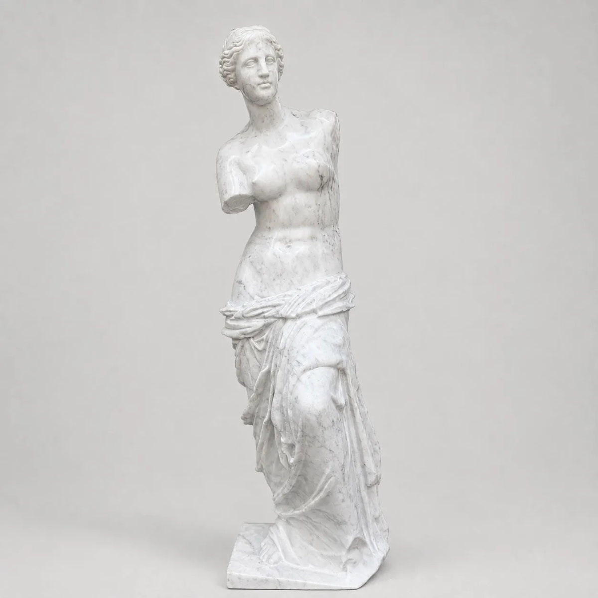 Venere di Milo in marmo di Carrara, vista frontale su fondo grigio chiaro.