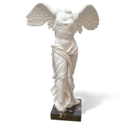 La statua della Vittoria Alata di Samotracia esposta in modo prominente, vista frontalmente, al Museo del Louvre.