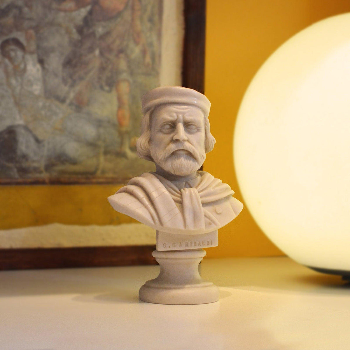 Busto di Giuseppe Garibaldi in marmo, accanto a una lampada sferica con un quadro sullo sfondo