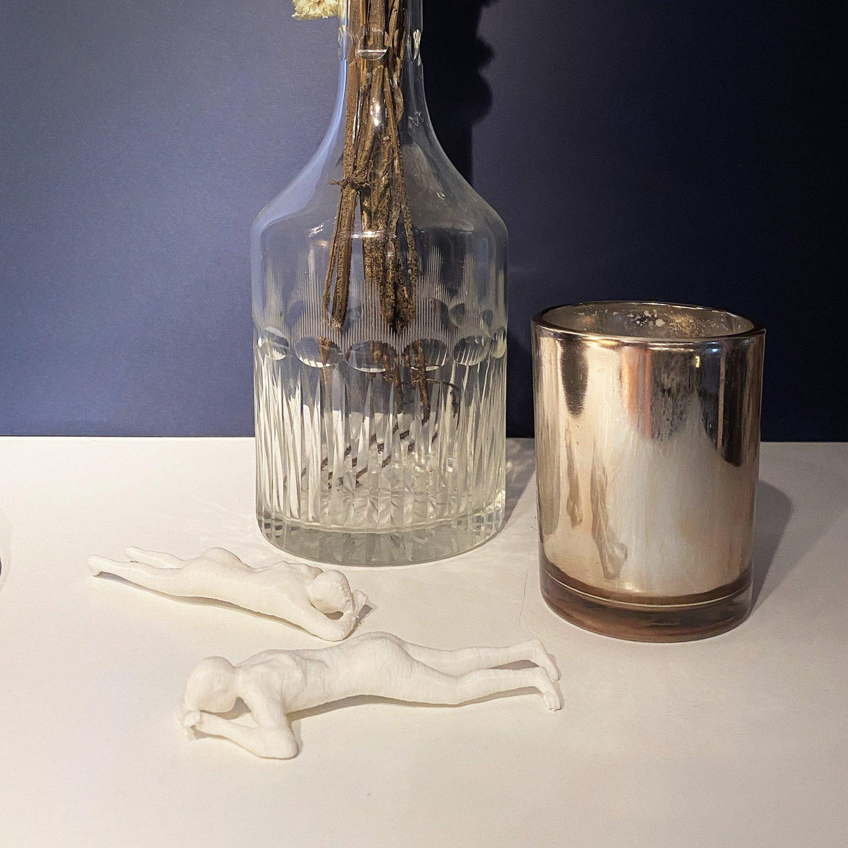Due riproduzioni bianche del calco di donna stesa in PLA su una console accanto a un vaso con fiori secchi.