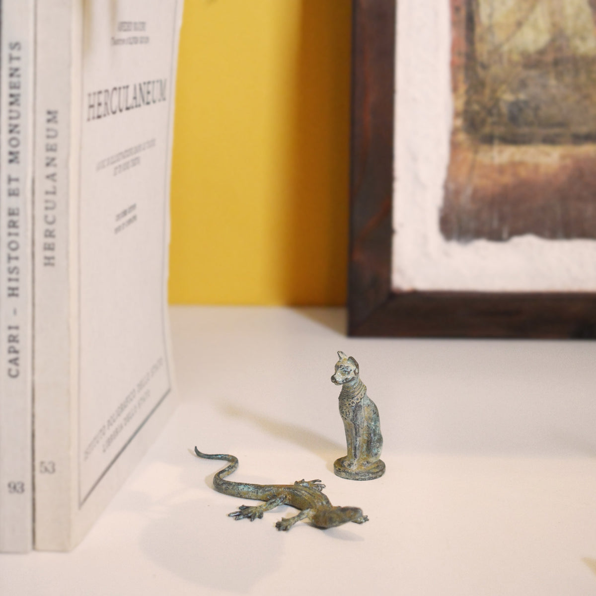 Gatto egizio e lucertola in bronzo su un ripiano bianco, accanto a libri