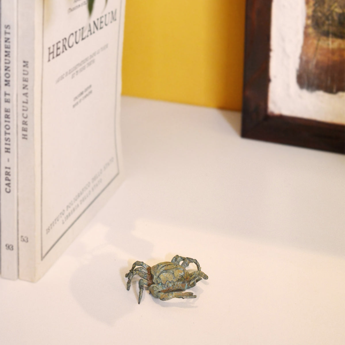 Granchio in bronzo con patina verde, statuetta decorativa con chele e zampe, fotografata in ambiente con libri e parete gialla sullo sfondo.
